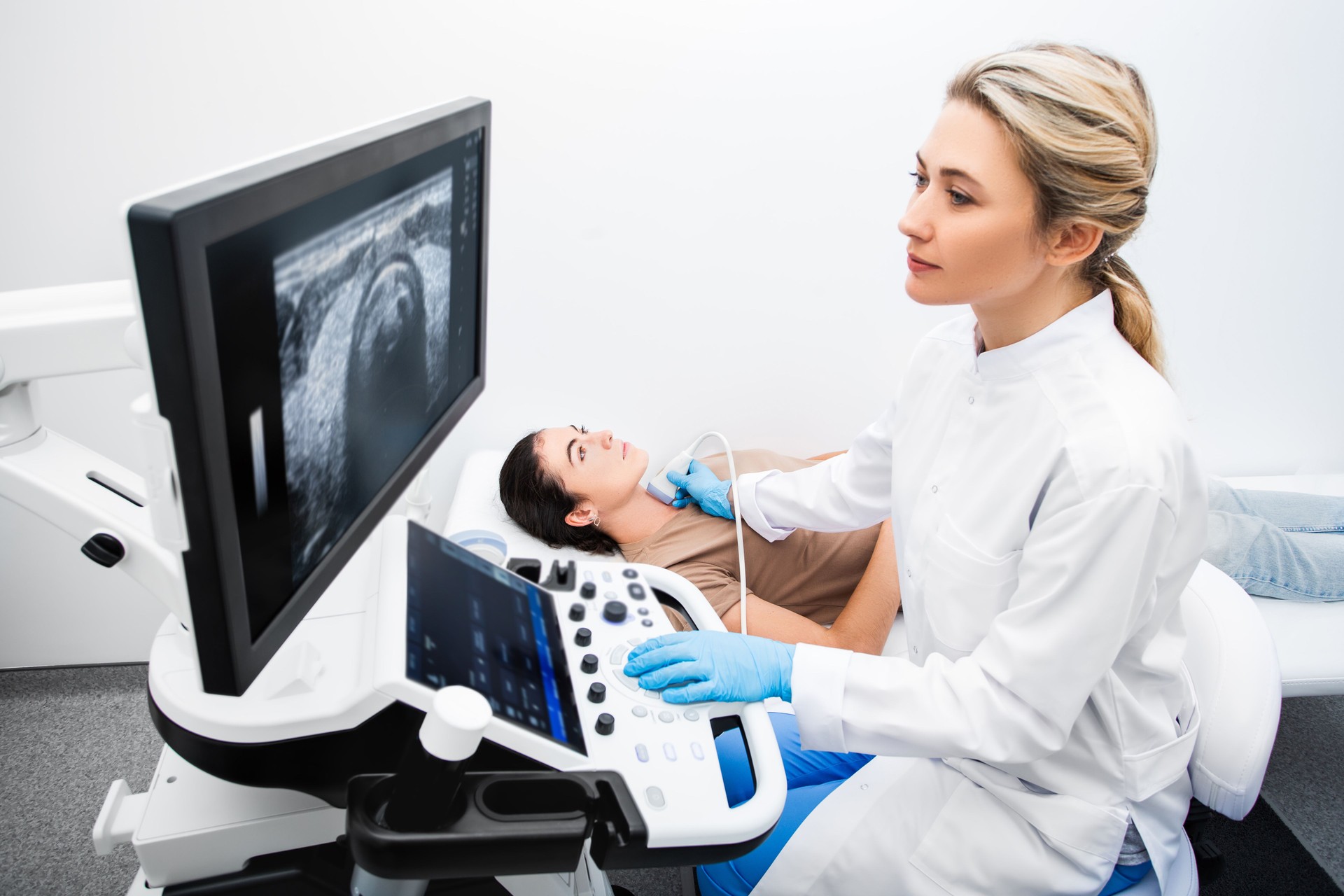 Woman endocrinologist making ultrasonography to a female patient in an ultrasound office. Ultrasound diagnostics of the thyroid gland.